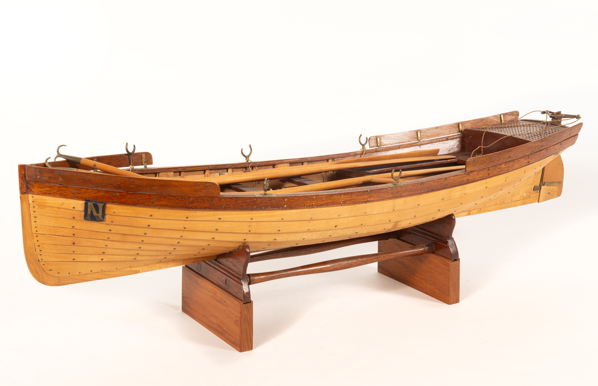 Gigg av 1834 års typ för korvetten Najaden. Bordlagd på spant, klink av bok, med fullständig inredning. 5 årtullar , 5 stycken åror, 1 mast, 2 båtshakar, 1 spri, 1 öskar. Roder med metallskädda. Skvättbord, trall och bänkar av mahogny.
Tillhört modellen "den gamla korvetten Najaden"