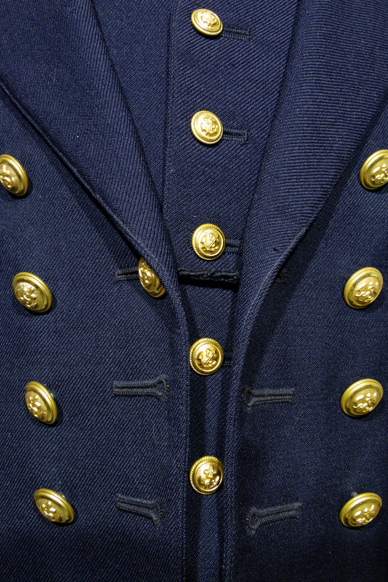 Uniformsjacka (marinen) till barn i mörkblått ylletyg. Försedd med fem rader av guldfärgade knappar med motiv av ankare. Ärmarna pryds av tre rader med guldfärgat band. Jackan är fodrar med ett svart tyg och ett randigt tyg med blå och bruna ränder på oblekt bas på ärmarnas insida. Jackan har en inneficka på höger sida. I jackans nackstycke finns en etikett med texten "Barngarderoben Falun" samt en hängare. 
