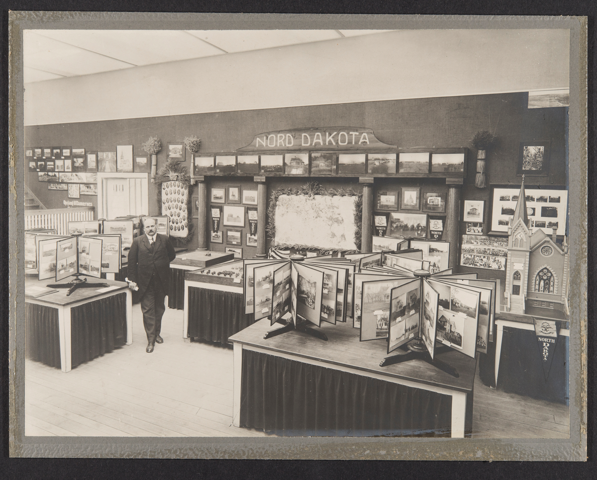 Oslo, 1914
Utstillingssal med fotografier, modeller m.m.
En mann inne i utstillingen.
Tekst: "Nord Dakota" "Det utflyttede Norges
utstilling 1914. Utstillingssalen".