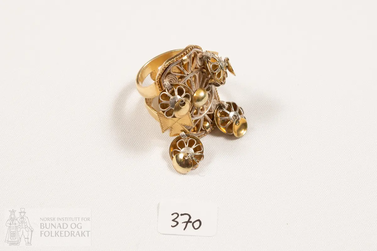 Fingerring. Forgylt sylvring. Dobbel ring med plate dekorert med filigransarbeid. Det same er dei 6 skålene.
Fleire stempel, blant anna 7 prikkar (Bergen bystempel), H.