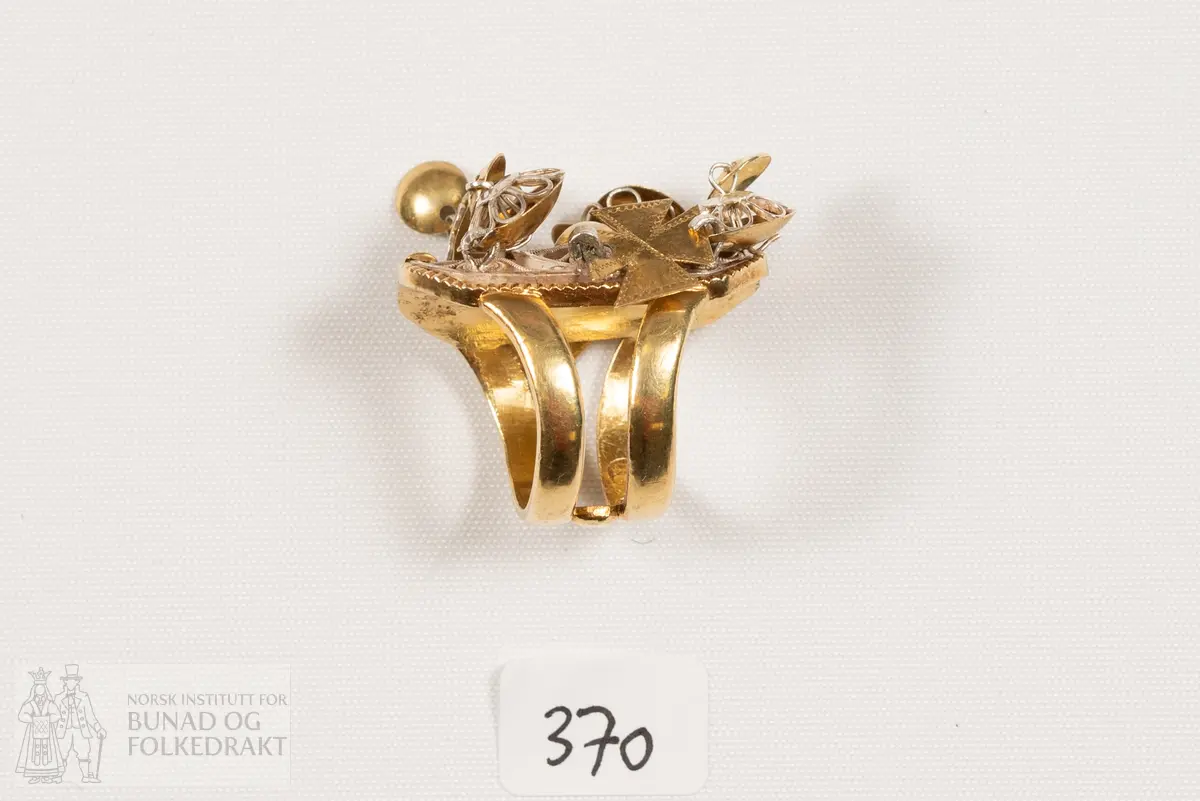 Fingerring. Forgylt sylvring. Dobbel ring med plate dekorert med filigransarbeid. Det same er dei 6 skålene.
Fleire stempel, blant anna 7 prikkar (Bergen bystempel), H.