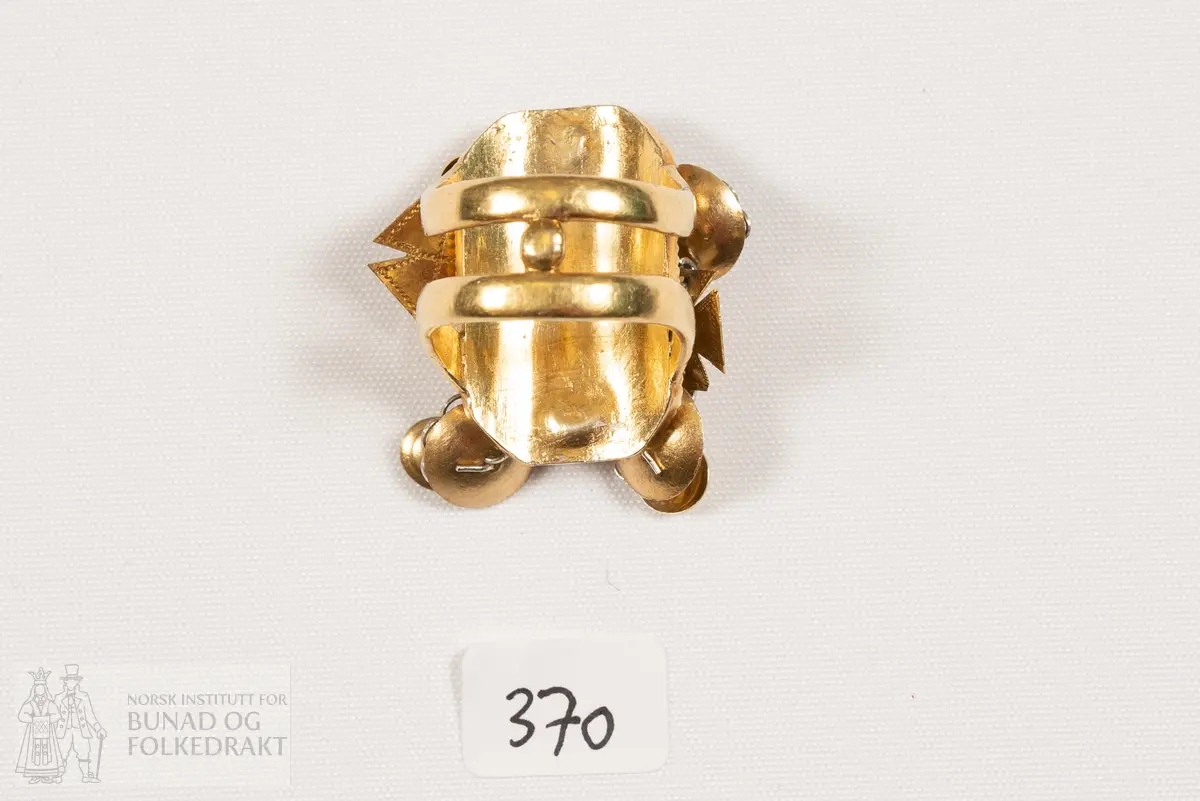 Fingerring. Forgylt sylvring. Dobbel ring med plate dekorert med filigransarbeid. Det same er dei 6 skålene.
Fleire stempel, blant anna 7 prikkar (Bergen bystempel), H.