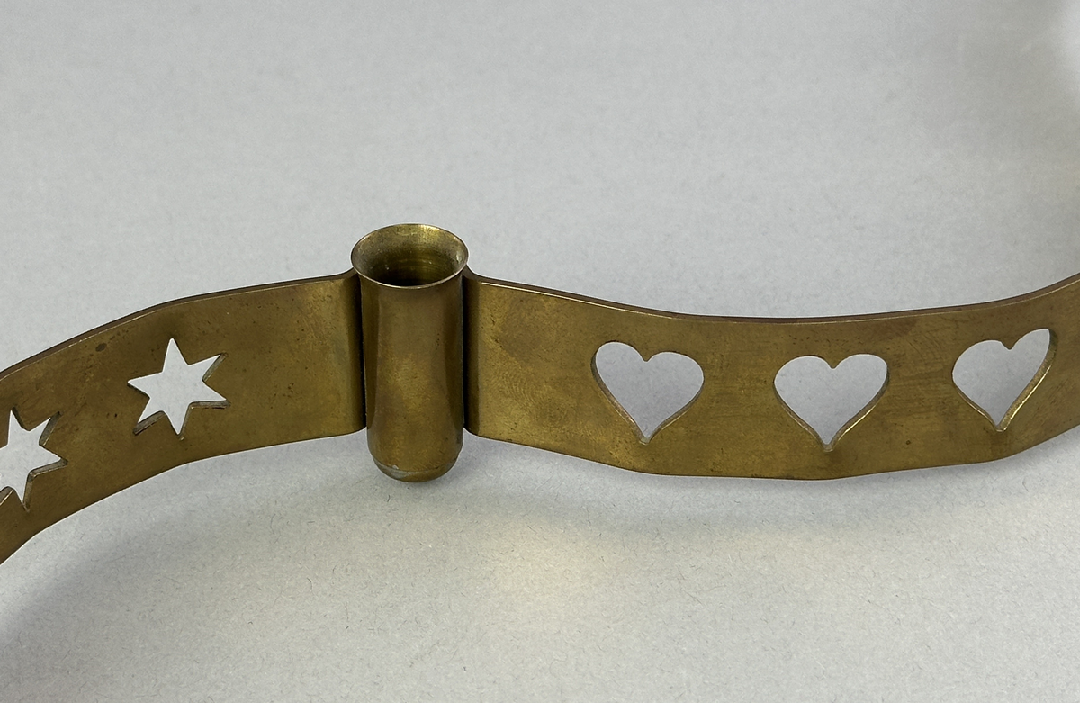 Ljusstake, "Slingan" för fyra ljus, består av ett mässingband som böjts i mjuk vågform och dekorerats med stansade stjärnor och hjärtan i grupper om fem. Mellan dessa grupper sitter ljushållare fastlödda med bandet.