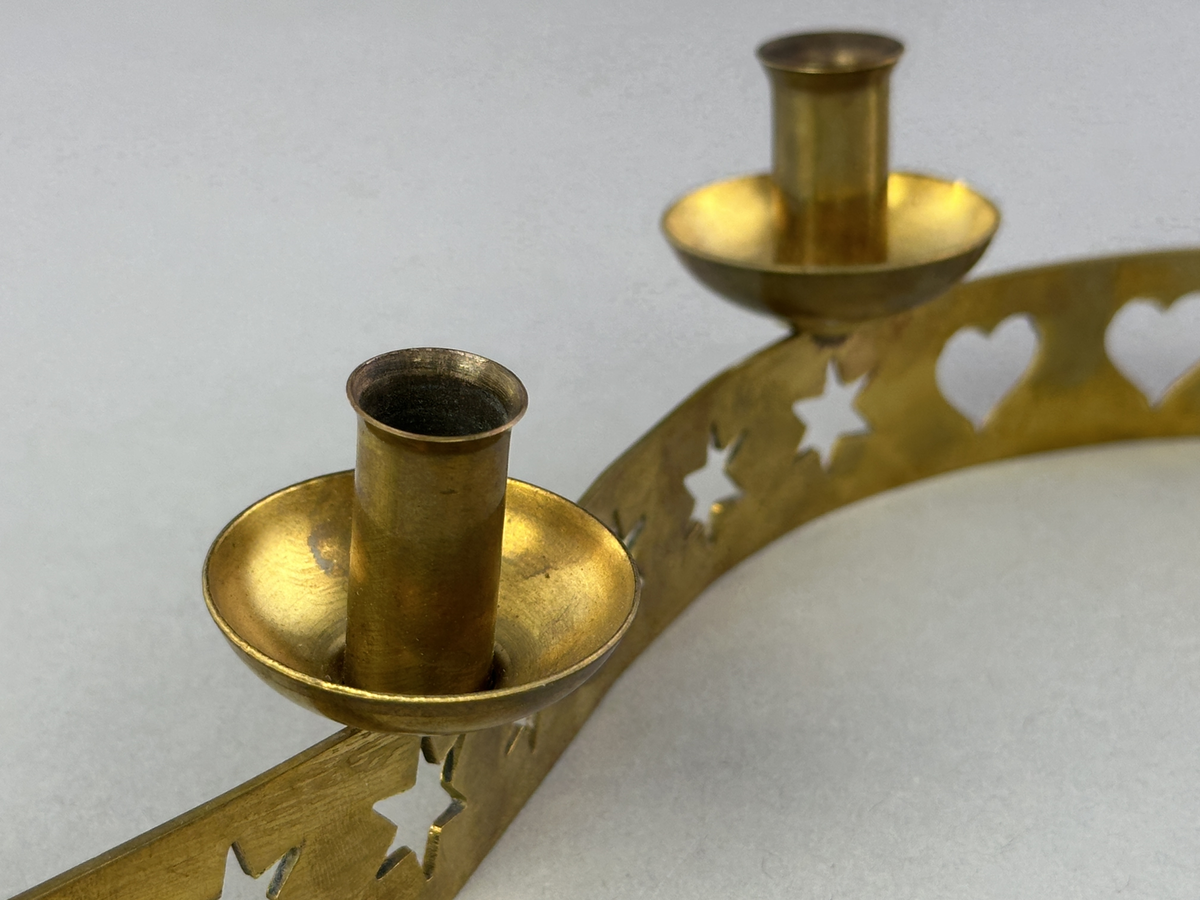 Ljusstake, "Ljusslingan" för sju ljus, består av ett mässingband som böjts i mjuk vågform och dekorerats med stansade stjärnor och hjärtan. Ljushållarna är fastlödda på bandets högkant.