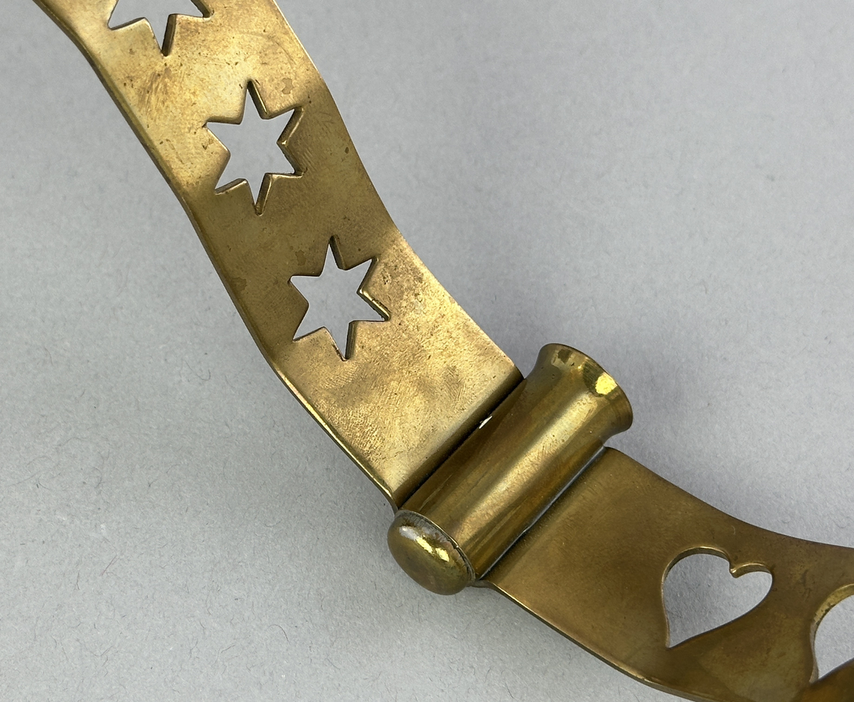 Ljusstake, "Slingan" för fyra ljus, består av ett mässingband som böjts i mjuk vågform och dekorerats med stansade stjärnor och hjärtan i grupper om fem. Mellan dessa grupper sitter ljushållare fastlödda med bandet.