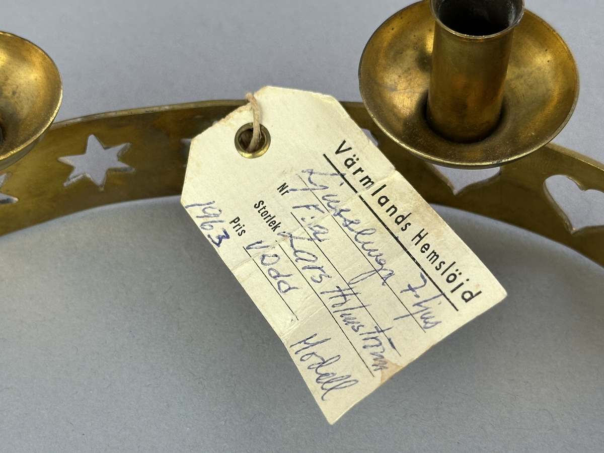 Ljusstake, "Ljusslingan" för sju ljus, består av ett mässingband som böjts i mjuk vågform och dekorerats med stansade stjärnor och hjärtan. Ljushållarna är fastlödda på bandets högkant.