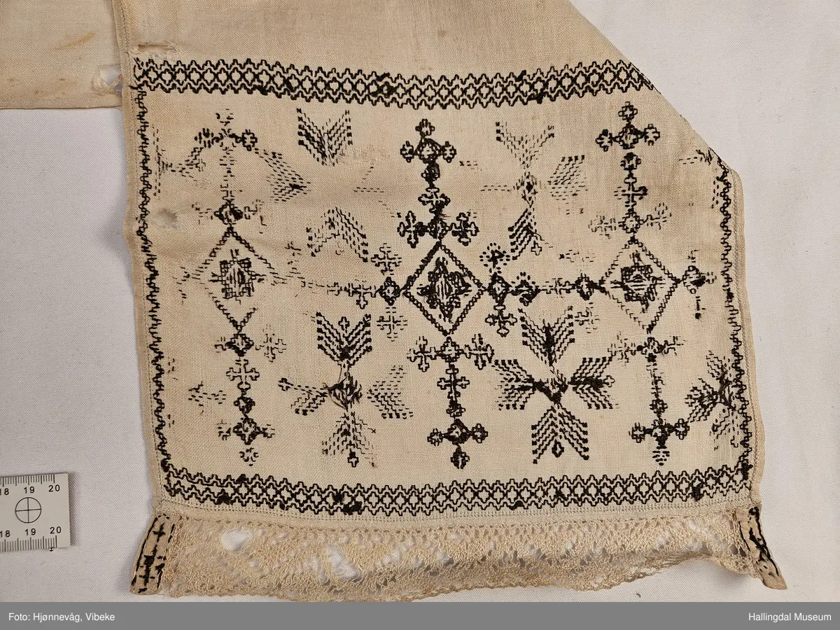 Lin, sauma, sydd. Sydd av 3 rektangulære stykke linty, i midten eit som er 54,0 x 54,0 cm, i kvar ende eit som er 29,5 x 26,8 cm. Svartsaum i ei lengde av 45 cm og br.: 2,7 cm langs eine langsida på midtstkket. Ytst på endestykka svartsaum i ei lengde av 19,2 cm over heile bredda. 3,2 cm breid blondekant langs båe stuttendane. 