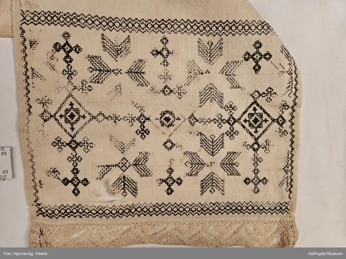 Lin, sauma, sydd. Sydd av 3 rektangulære stykke linty, i midten eit som er 54,0 x 54,0 cm, i kvar ende eit som er 29,5 x 26,8 cm. Svartsaum i ei lengde av 45 cm og br.: 2,7 cm langs eine langsida på midtstkket. Ytst på endestykka svartsaum i ei lengde av 19,2 cm over heile bredda. 3,2 cm breid blondekant langs båe stuttendane. 