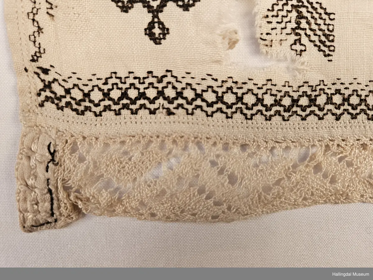 Lin, sauma, sydd. Sydd av 3 rektangulære stykke linty, i midten eit som er 54,0 x 54,0 cm, i kvar ende eit som er 29,5 x 26,8 cm. Svartsaum i ei lengde av 45 cm og br.: 2,7 cm langs eine langsida på midtstkket. Ytst på endestykka svartsaum i ei lengde av 19,2 cm over heile bredda. 3,2 cm breid blondekant langs båe stuttendane. 