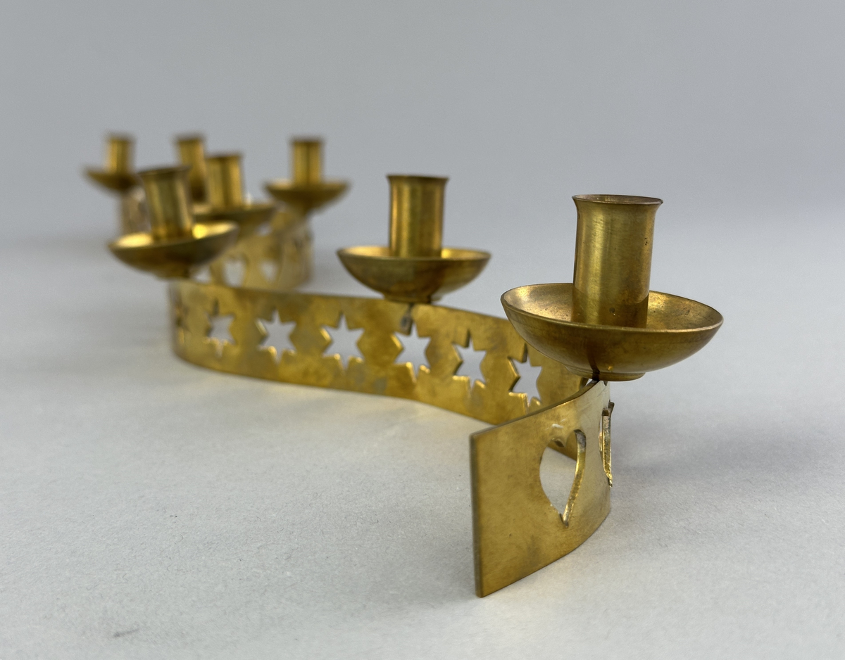 Ljusstake, "Ljusslingan" för sju ljus, består av ett mässingband som böjts i mjuk vågform och dekorerats med stansade stjärnor och hjärtan. Ljushållarna är fastlödda på bandets högkant.