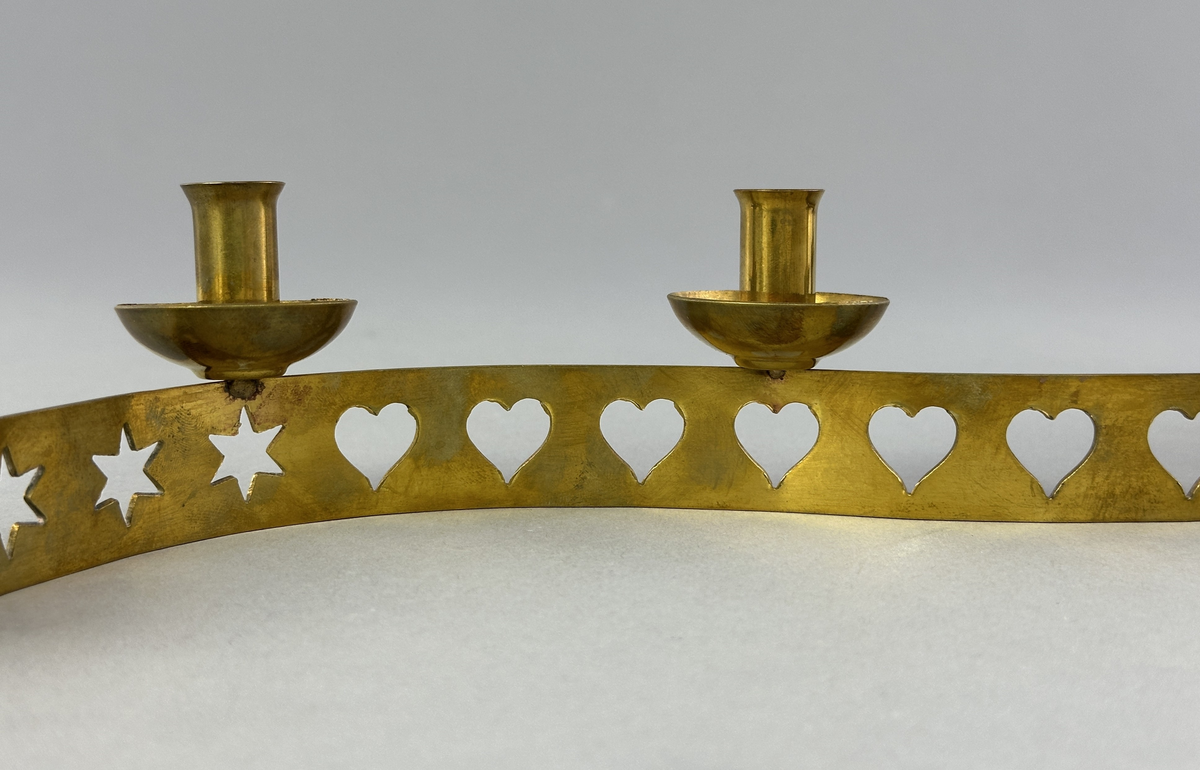 Ljusstake, "Ljusslingan" för sju ljus, består av ett mässingband som böjts i mjuk vågform och dekorerats med stansade stjärnor och hjärtan. Ljushållarna är fastlödda på bandets högkant.