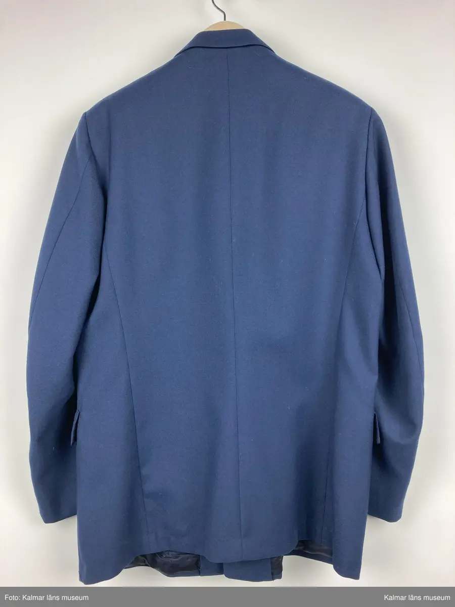 KLM 44463:9. Kavaj. Uniformsjacka för stins, SJ. Storlek C54. Av kypertvävt mörkblått ylle. Krage och slag. Knäpps fram med fyra st. knappar av gulmetall med SJ vapen på. Fickor med ficklock samt bröstficka, på vänster framstycke. Fodrad med mörkblått tyg i livet och grått i ärmen. Hank i nacken. Innerfickor på båda framstyckena. Textiletikett vid höger innerficka med vävd text: CBV C54 KARLSKRONA.  
Kavajen är av tunnare sort och har ev. använts som sommar kavaj till byxor KLM 44463:8:2 och väst KLM 44463:8:3.