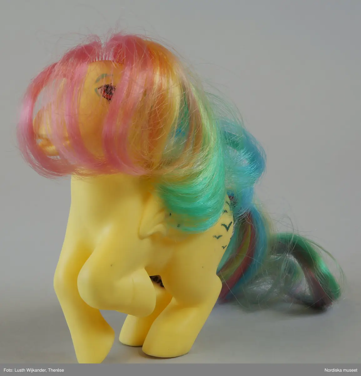 Inventering Sesam 1996-1999:
H 14  L 12   cm
Häst, leksak, "My little pony", gjuten gul plast, lång man och svans av konstfiber i regnbågensfärger, gröna fåglar på länden. 
Märkt under hovarna "Hasbro pat. pend. Hong Kong".
inköpt i samband med 1986 års hemundersökning.
Kerstin Körnemark 1986
