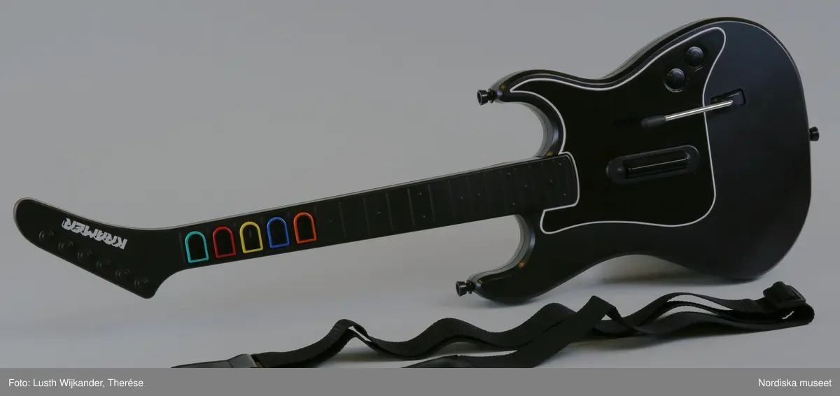 TV-spelet "Guitar Hero III Legends of Rock" med förpackning. 
a+) Elgitarr med avtagbar hals, av svart plast, svart axelrem av syntettextil med konstläder (plast) och plastöglor.
b+) 2 ark med klisterbilder att fästa på gitarren
c) Broschyr med instruktioner om funktion och säkerhet på flera olika språk.
d) Fodral av blå plast med inplastat omslag av papper med text. På framsidan "Playstation 2 / Guitarr Hero III LEGENDS of ROCK" och bild på hårdrockare. Baksidan bl.a. "SLÄPP LOSS DIN INRE ROCKLEGEND / Över 70 rockiga låtar.".
e) CD-skiva med programvara (förvarad i fodral d).
f) Instruktionsbok på de nordiska spårken (förvarad i fodral d) 
g+) Förpackning av papp. Ytterfodral med text och bilder. Inre lådan med inredning för de olika delarna.
 
Tv-spelet är avsett för spelplattformen Playstation 2, vilket är en vanlig spelplattform. Spelet går ut på att det spelas upp en låt (man väljer själv låt och nivå) och ska sedan försöka spela på gitarren genom att trycka på knapparna och på så vis lyckas spela samma ton som musiken spelar samtidigt.

Vid förvärvet avlägsnades plastpåsar som del av a och b låg i, samt två 1.5volts-batterier av märket Duracell som låg i gitarren, då de ej bedömdes möjliga att spara. Även fyra papperspåsar med Silicagel (för att hindra att fukt skadar elektronik mm) togs bort.

Nyinköp den 2008-02-20 för att rekonstruera julkklappsönskemål julen 2007 från Erik Thomelius född 1999, Vaxholm. Inköpt av Nordiska museet för 439 kr. Ingår i projektet "Barn tar plats". Se dokumentation i arkivet D455.
/Ulf Hamilton 2008-05-27     