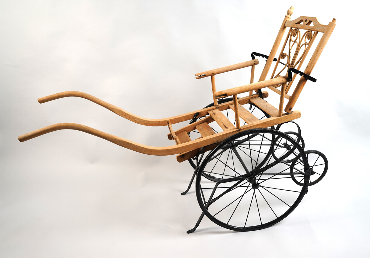 Rullestol til barn. I tre og metall. Til å køyre (handtak framme) av ein annan person enn den som sit i stolen. To par hjul (store framme, små bak), fotstøtte og armlener. Vinkel på rygglene kan regulerast i tre trinn. Spinkle (smale) hjulringar (felgar).
Øvre del (sitteplata med rygglene, armlener og fotstøtte og handtaka) i tre. 
Nedre del (og bøyle med reguleringstrinn bak rygg) i metall (utan hjulringane som er i tre, men med metall skoning rundt). Spilar og akslingar i hjula av metall. 
Fotstøtte i tre, som kan vippast opp og ned. Ryggen kan stillast i tre stiller (metall bøyle). I ryggen er innfelt dekorativt forma bøygde tremateriale.