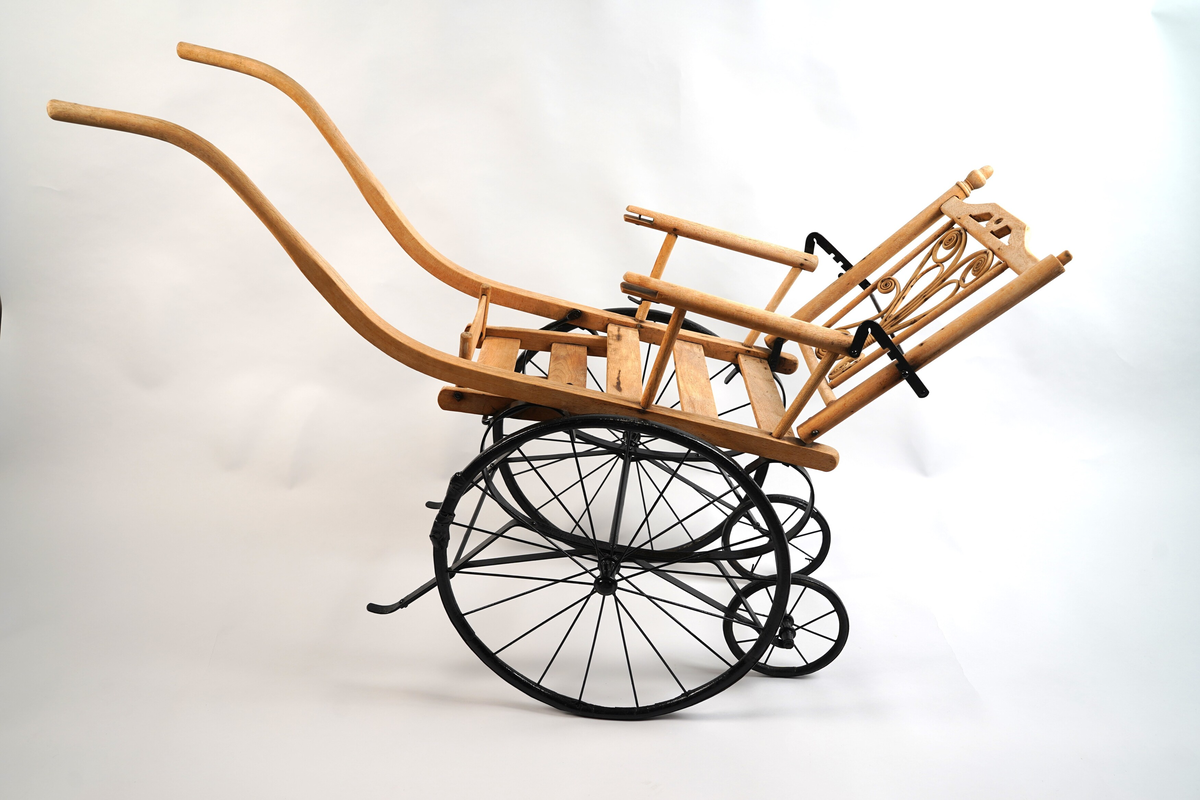 Rullestol til barn. I tre og metall. Til å køyre (handtak framme) av ein annan person enn den som sit i stolen. To par hjul (store framme, små bak), fotstøtte og armlener. Vinkel på rygglene kan regulerast i tre trinn. Spinkle (smale) hjulringar (felgar).
Øvre del (sitteplata med rygglene, armlener og fotstøtte og handtaka) i tre. 
Nedre del (og bøyle med reguleringstrinn bak rygg) i metall (utan hjulringane som er i tre, men med metall skoning rundt). Spilar og akslingar i hjula av metall. 
Fotstøtte i tre, som kan vippast opp og ned. Ryggen kan stillast i tre stiller (metall bøyle). I ryggen er innfelt dekorativt forma bøygde tremateriale.