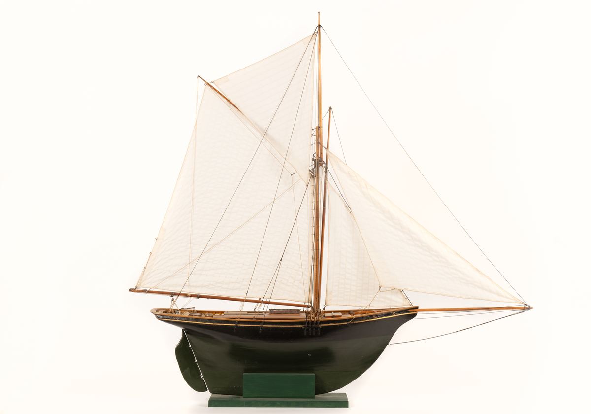 Båtmodell av segelkuttern HELMI, byggd i ett stycke med däcksinredning oc överhängande stäv. Akterspegel med hackbräde. Roder med rorkult av järn. Riggad, mast med stång, gaffelsegel, fock och klyvare. Svartmålad, förgylld list, grön vattengång. Fernissat däck. Tillhörande monter: svart.