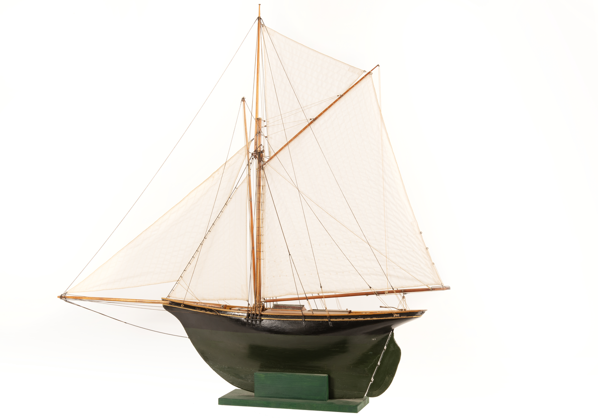 Båtmodell av segelkuttern HELMI, byggd i ett stycke med däcksinredning oc överhängande stäv. Akterspegel med hackbräde. Roder med rorkult av järn. Riggad, mast med stång, gaffelsegel, fock och klyvare. Svartmålad, förgylld list, grön vattengång. Fernissat däck. Tillhörande monter: svart.