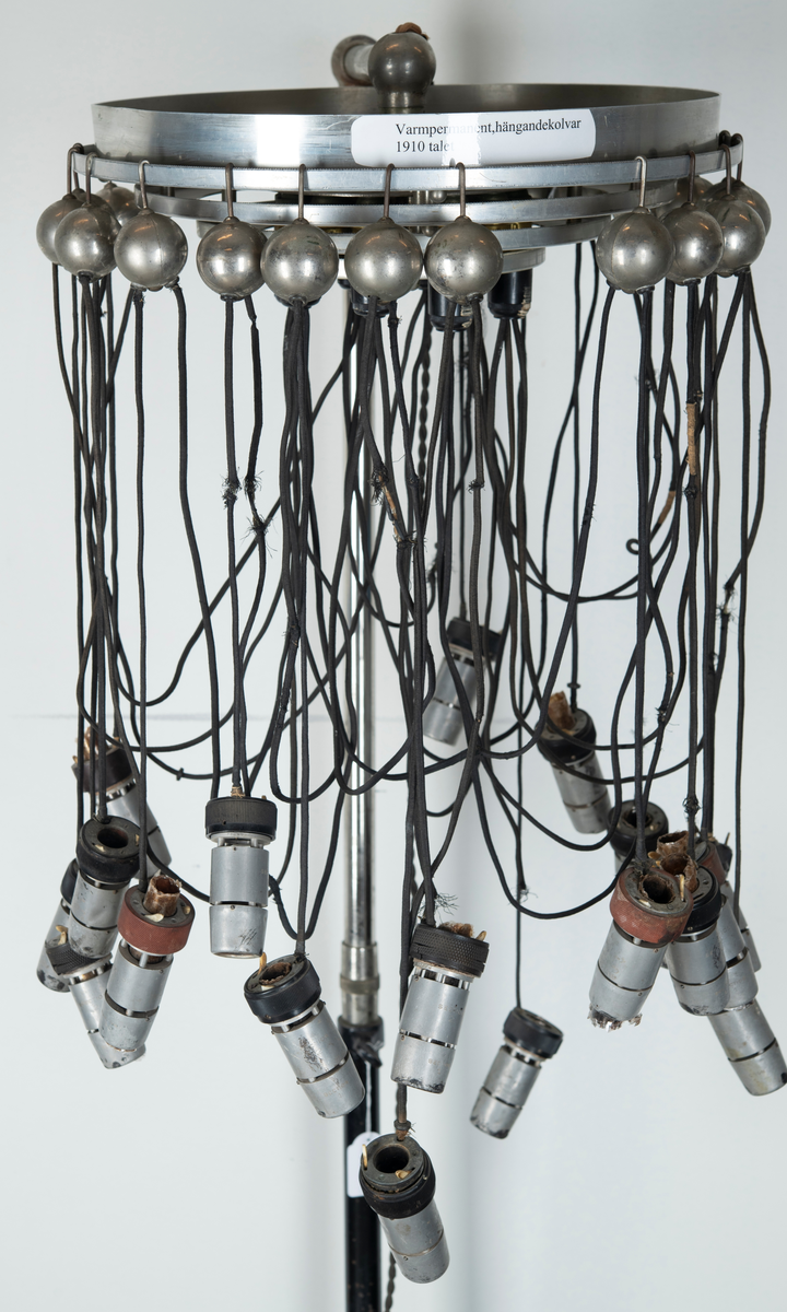 Skriv om texten
sittande på arm av metall som skjuter ut från  ett äggformat hölje av plåt inom vilken torkapparatens motor sitter. På toppen en dekorativ formation av blått glas på vilken det står instansat. "Wella" samt fabrikatets logotyp i form av ett kvinnohuvud med långt hår. På utsidan bockade stålrör som vilka man kan ta tag i som handtag när man vill förflytta torken. På ena sidan sitter ena änden av en elektrisk kabel av vit plast i vars andra ände en stickkontakt av svart plast sitter. Vid användning av apparaten sticks denna i vägguttag så att ström tillförs och maskinen kan användas. Det hela sitter på en ställing bestående av vertikalt stående stålrör av metall med fyrarmad fot med hjul så att ställningen kan förflyttas lätt. Stålröret är tvådelat med den ena delen instucken i den andra och med hjälp av en skruv av plast kan ställas i olika höjd. Metallskylt med text: Wella Darmstadt" samt upplysningar för typ, nr, strömstyrka. På plasthuvens utsida en något böjd och deformerad skylt i form av utskurna silverfärgade bokstäver i plast: "Wellapot". Placeras ovanför en sittande persons huvud för att torka håret med.