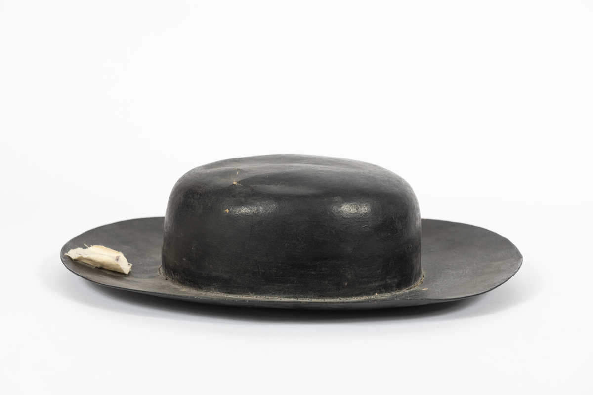 Hatt av papp. Svartmålad med rödaktigt innerfoder.