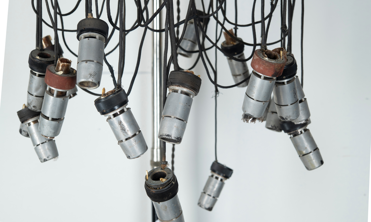 Skriv om texten
sittande på arm av metall som skjuter ut från  ett äggformat hölje av plåt inom vilken torkapparatens motor sitter. På toppen en dekorativ formation av blått glas på vilken det står instansat. "Wella" samt fabrikatets logotyp i form av ett kvinnohuvud med långt hår. På utsidan bockade stålrör som vilka man kan ta tag i som handtag när man vill förflytta torken. På ena sidan sitter ena änden av en elektrisk kabel av vit plast i vars andra ände en stickkontakt av svart plast sitter. Vid användning av apparaten sticks denna i vägguttag så att ström tillförs och maskinen kan användas. Det hela sitter på en ställing bestående av vertikalt stående stålrör av metall med fyrarmad fot med hjul så att ställningen kan förflyttas lätt. Stålröret är tvådelat med den ena delen instucken i den andra och med hjälp av en skruv av plast kan ställas i olika höjd. Metallskylt med text: Wella Darmstadt" samt upplysningar för typ, nr, strömstyrka. På plasthuvens utsida en något böjd och deformerad skylt i form av utskurna silverfärgade bokstäver i plast: "Wellapot". Placeras ovanför en sittande persons huvud för att torka håret med.