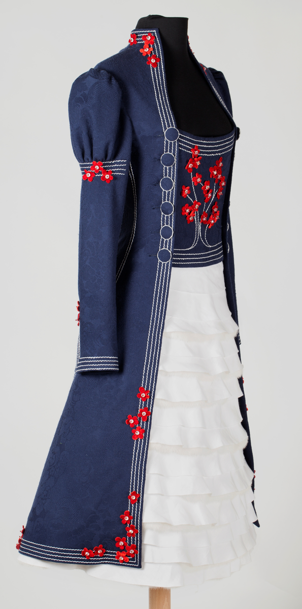 Frontal smekke med sentralt plassert, brodert tre eller grener med påsydde småblomster. Parallelle stikninger i kontrasterende farge, ispedd tilsvarende småblomster.