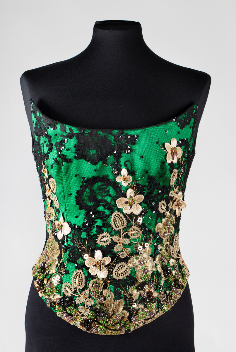 Småblomster og blader som vokser opp av en blomstereng, alt av gull, mot en bakgrunn av storblomstret tyllblonde.