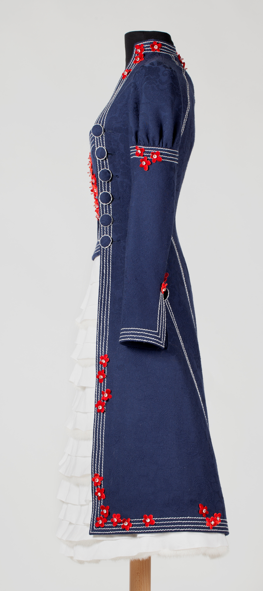 Frontal smekke med sentralt plassert, brodert tre eller grener med påsydde småblomster. Parallelle stikninger i kontrasterende farge, ispedd tilsvarende småblomster.