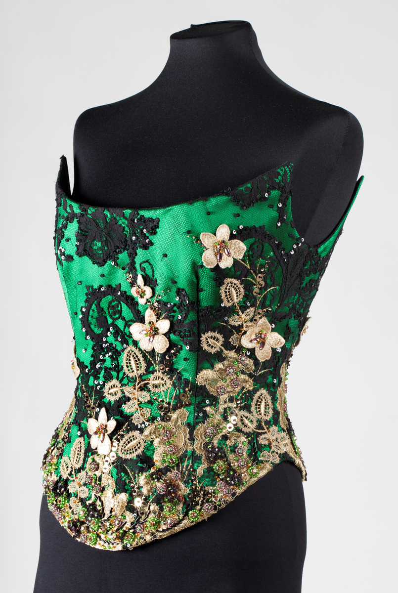 Småblomster og blader som vokser opp av en blomstereng, alt av gull, mot en bakgrunn av storblomstret tyllblonde.