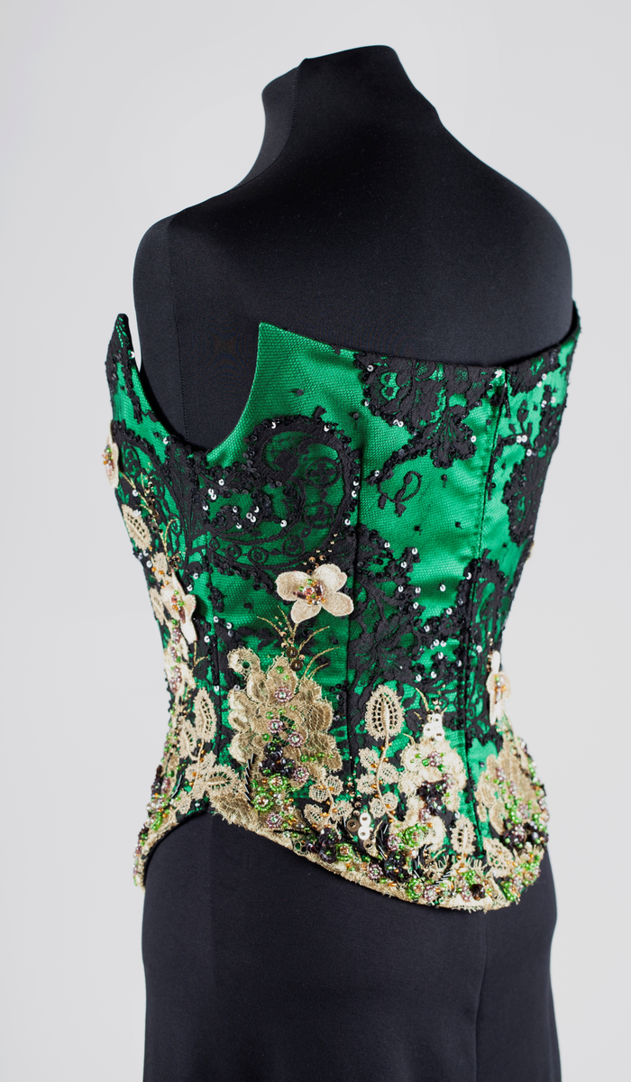 Småblomster og blader som vokser opp av en blomstereng, alt av gull, mot en bakgrunn av storblomstret tyllblonde.