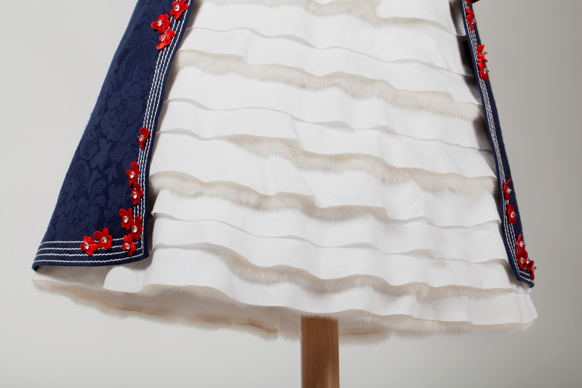 Frontal smekke med sentralt plassert, brodert tre eller grener med påsydde småblomster. Parallelle stikninger i kontrasterende farge, ispedd tilsvarende småblomster.