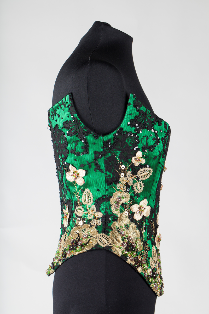 Småblomster og blader som vokser opp av en blomstereng, alt av gull, mot en bakgrunn av storblomstret tyllblonde.