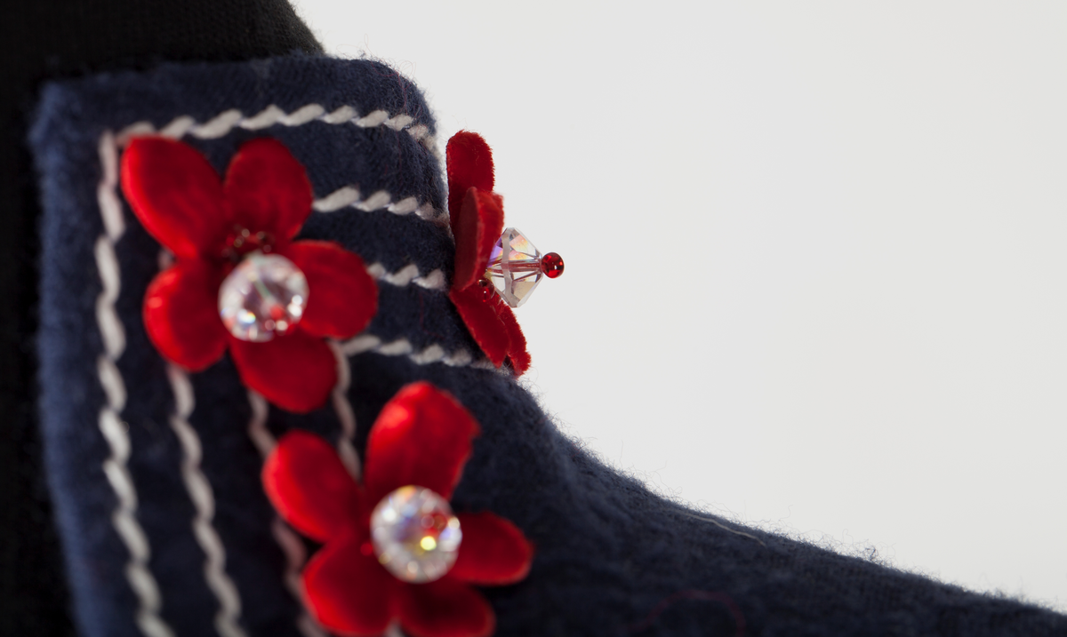 Frontal smekke med sentralt plassert, brodert tre eller grener med påsydde småblomster. Parallelle stikninger i kontrasterende farge, ispedd tilsvarende småblomster.