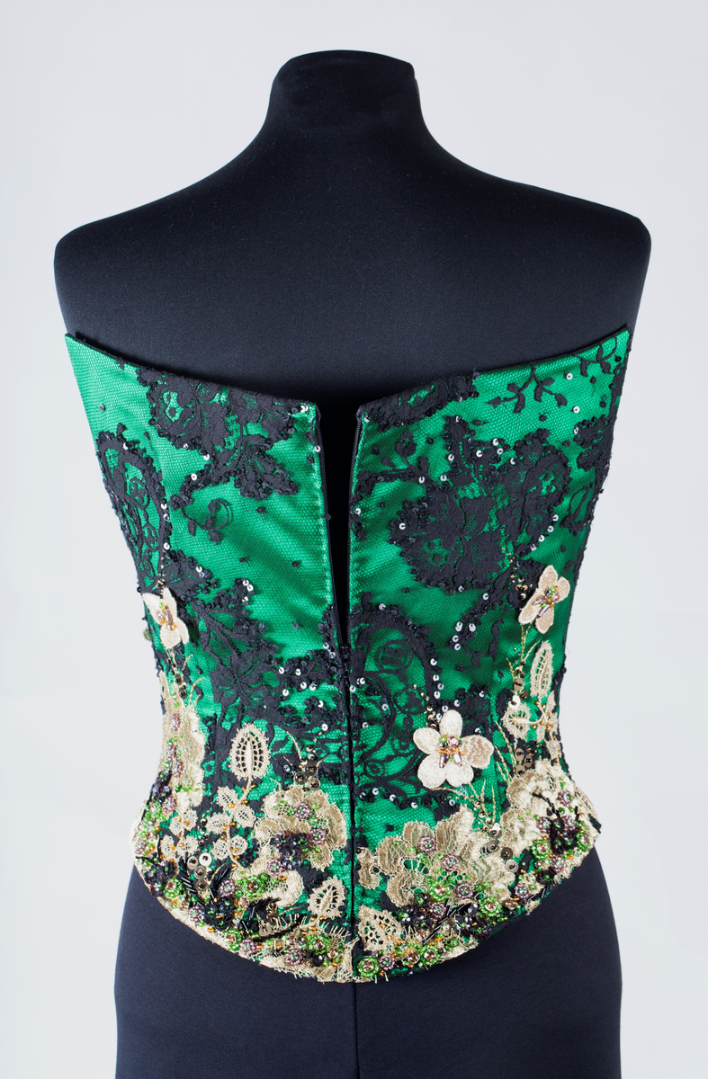 Småblomster og blader som vokser opp av en blomstereng, alt av gull, mot en bakgrunn av storblomstret tyllblonde.