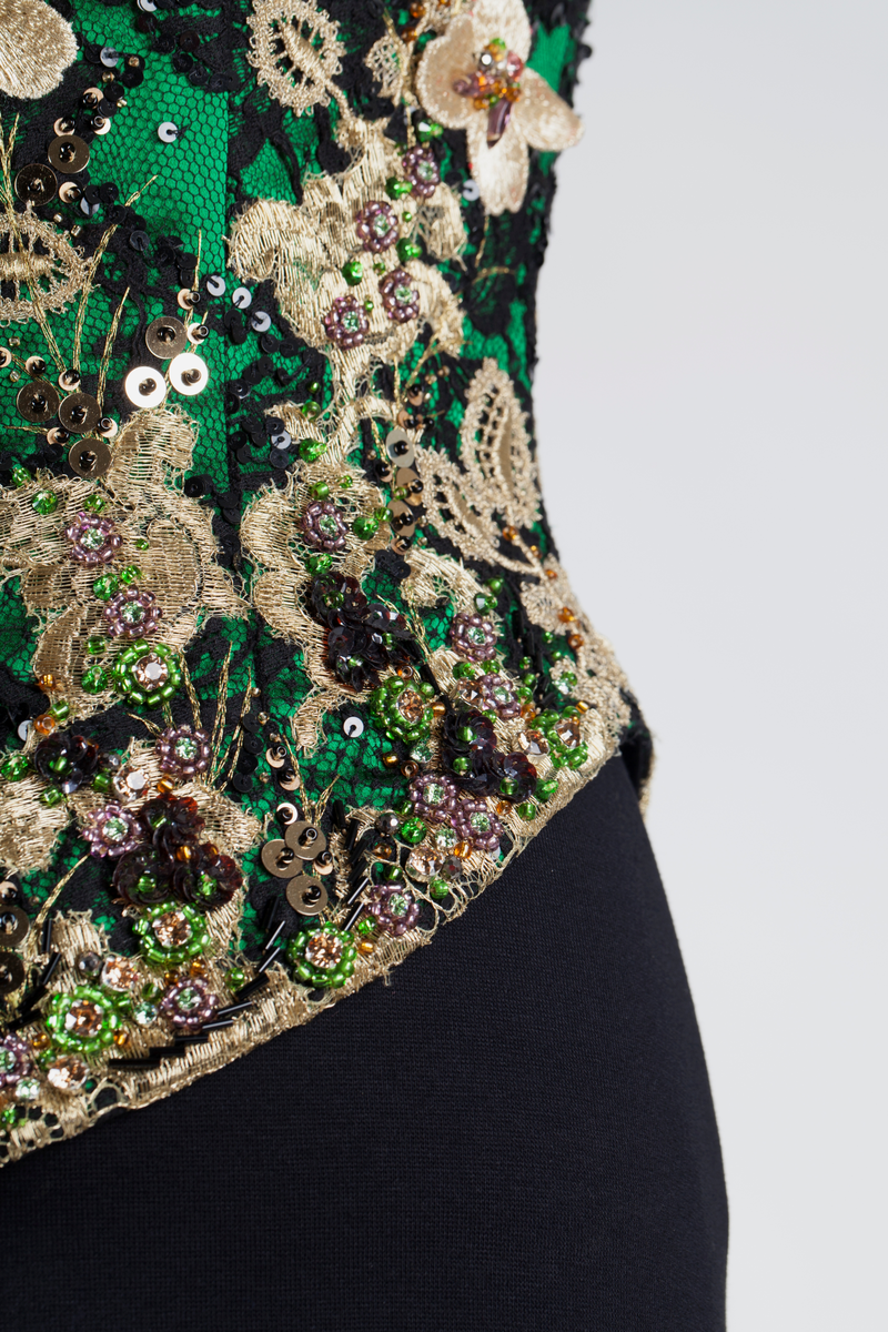 Småblomster og blader som vokser opp av en blomstereng, alt av gull, mot en bakgrunn av storblomstret tyllblonde.