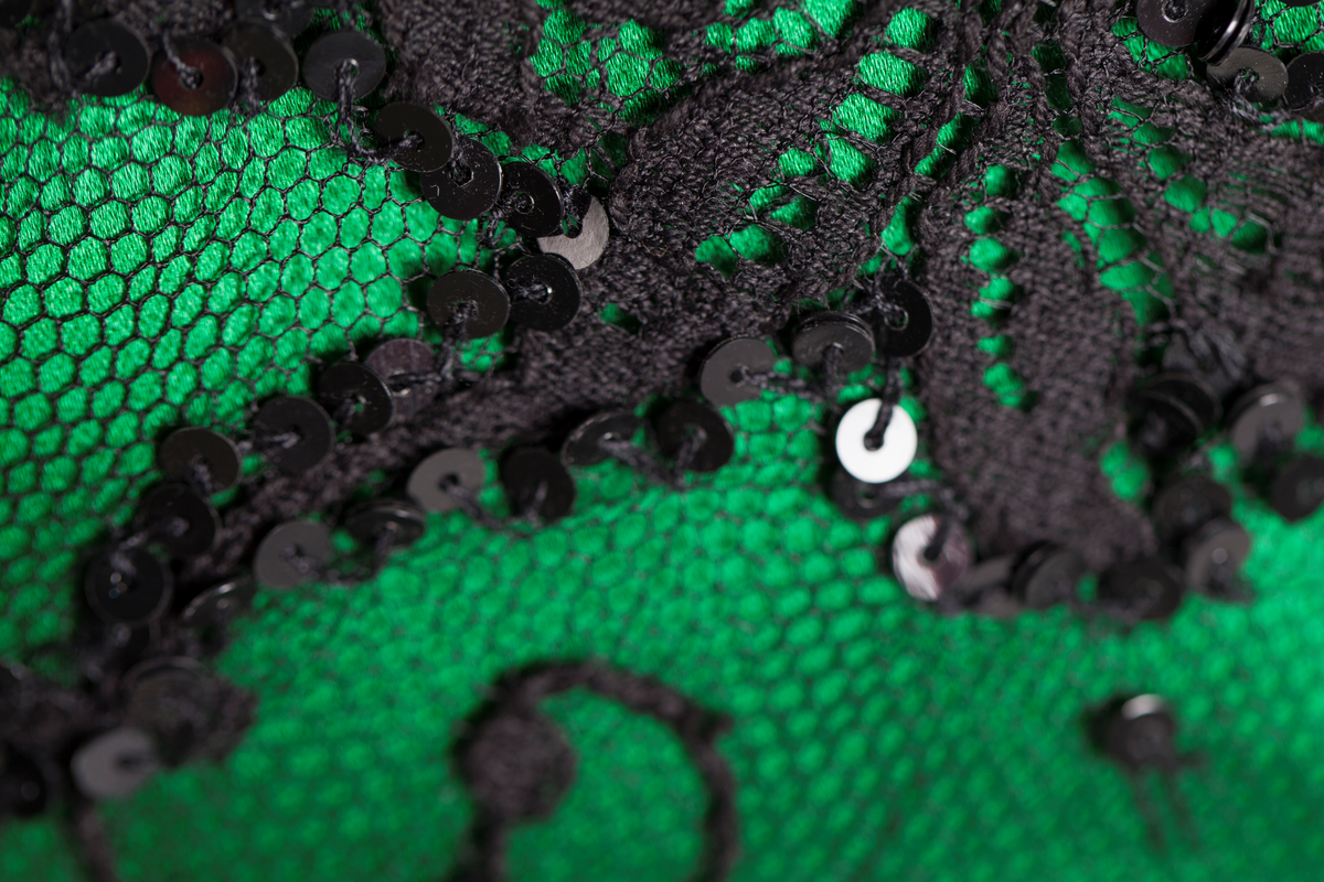 Småblomster og blader som vokser opp av en blomstereng, alt av gull, mot en bakgrunn av storblomstret tyllblonde.