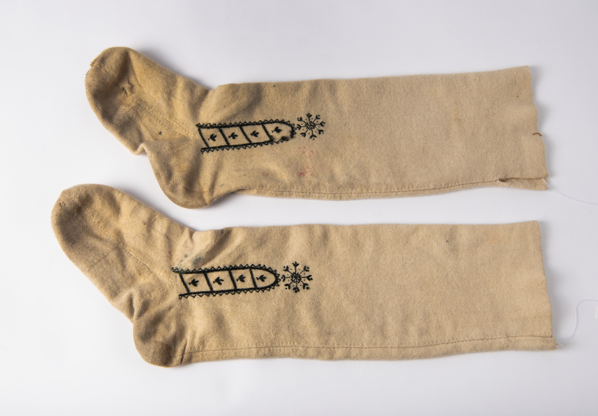 Hvite sydde strømper av vadmel med brodert dekor i svart.