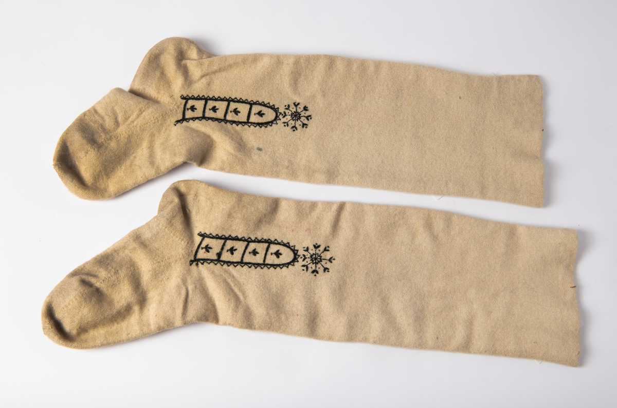 Hvite sydde strømper av vadmel med brodert dekor i svart.