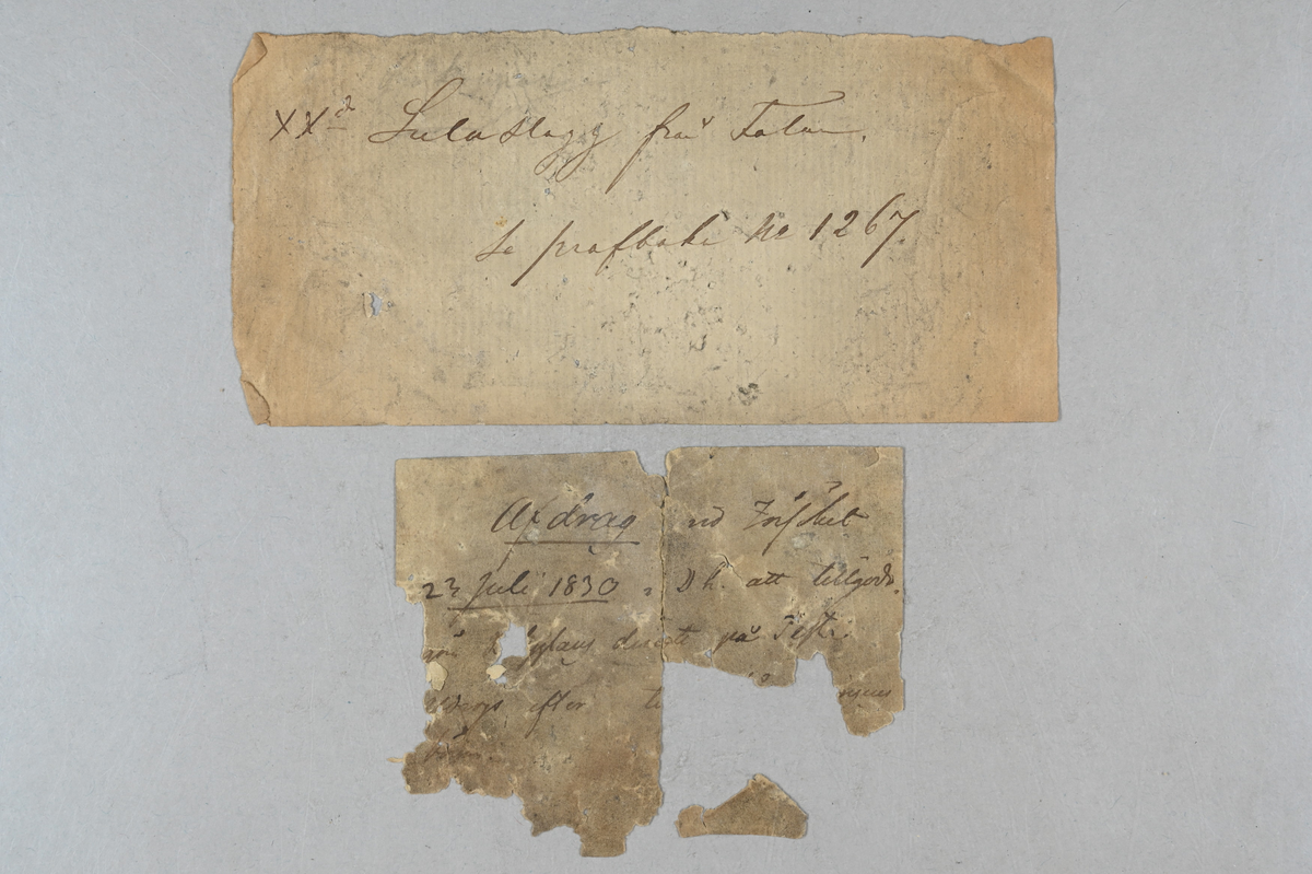 Materialprov, gråaktig. Två medföljande lappar med notering: "Afdrag vid försöket 23 juli 1830 i D h att tillgodo(...)" och "xx2 (?) Suluslagg från Falun. Se profboken 1267."