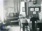 Rumsinteriör med piano och pianopall, bord och stolar, draperier och i rummet intill syns en soffa och karmstolar mm. troligen från Centralpalatset i Gävle stad.