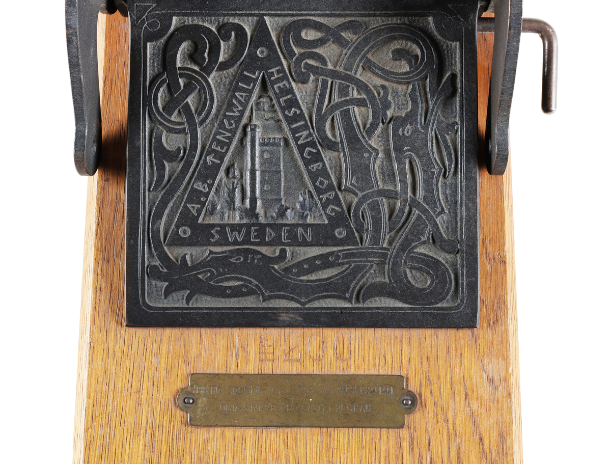 Hålstans med reliefdekor föreställande "fästningen kärnan" inom triangel och omgiven av drakslingor. Styrskena för olika pappersstorlekar. Märkt: A.B. TENGWALL HELSINGBORG SWEDEN No 200. 

Äldre historik:
Kärnan är ett torn som är den enda kvarstående byggnaden av det medeltida Helsingborgs slott. Dendrokronologisk datering har visat att Kärnan byggdes på 1310-talet, då Erik Menved var kung i Danmark. Tornet är 35 meter högt och ligger i sin tur på landborgen. (Wikipedia)

Proveniens: Oscar Jacobson AB, Borås.

Äldre historik:
Oscar Jacobson är ett svenskt herrkonfektionsföretag grundat i Borås 1903 av skräddaren Oscar Jacobson. Oscar Jacobson var VD i företaget fram till 1957 då han efterträddes av sin son Anders Jacobson. Familjen Jacobson sålde 1971 företaget till Sweteco. (Wikipedia)