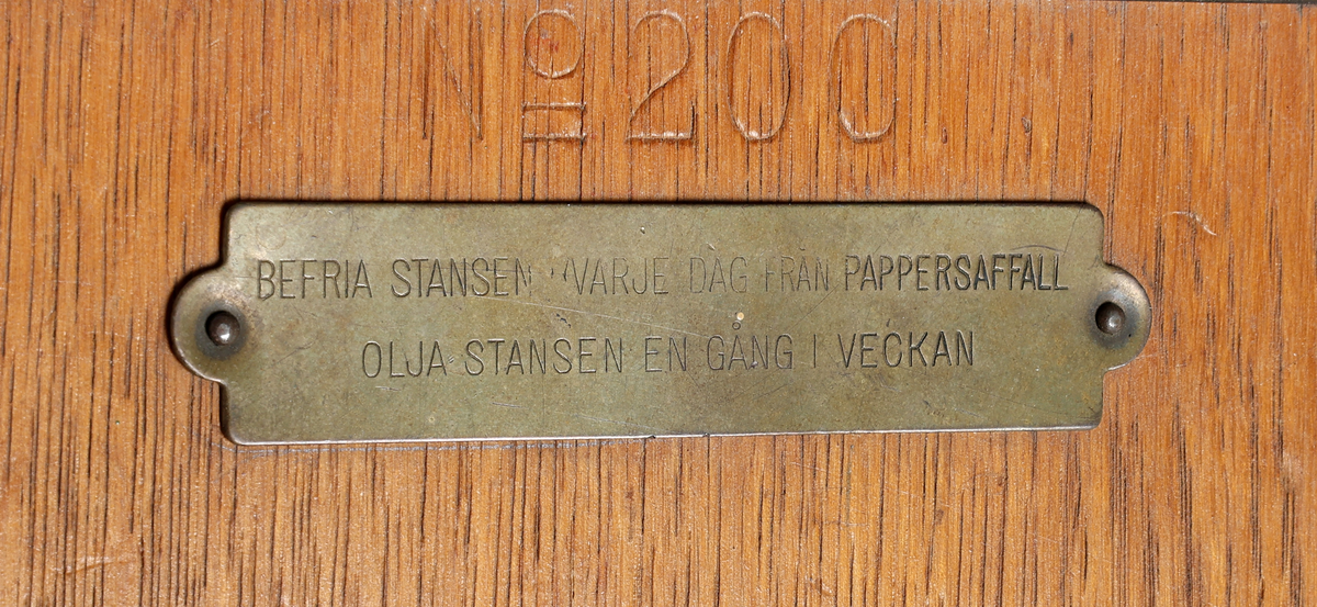 Hålstans med reliefdekor föreställande "fästningen kärnan" inom triangel och omgiven av drakslingor. Styrskena för olika pappersstorlekar. Märkt: A.B. TENGWALL HELSINGBORG SWEDEN No 200. 

Äldre historik:
Kärnan är ett torn som är den enda kvarstående byggnaden av det medeltida Helsingborgs slott. Dendrokronologisk datering har visat att Kärnan byggdes på 1310-talet, då Erik Menved var kung i Danmark. Tornet är 35 meter högt och ligger i sin tur på landborgen. (Wikipedia)

Proveniens: Oscar Jacobson AB, Borås.

Äldre historik:
Oscar Jacobson är ett svenskt herrkonfektionsföretag grundat i Borås 1903 av skräddaren Oscar Jacobson. Oscar Jacobson var VD i företaget fram till 1957 då han efterträddes av sin son Anders Jacobson. Familjen Jacobson sålde 1971 företaget till Sweteco. (Wikipedia)