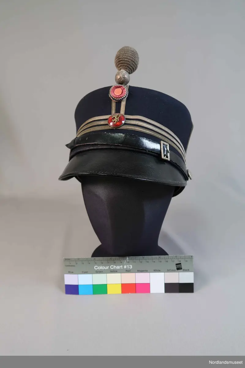 Uniformslue for politiet. Emaljert merke med riksløve. Skinnsnor. Den har en kule som sitter i front.