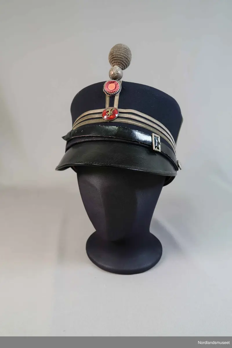 Uniformslue for politiet. Emaljert merke med riksløve. Skinnsnor. Den har en kule som sitter i front.