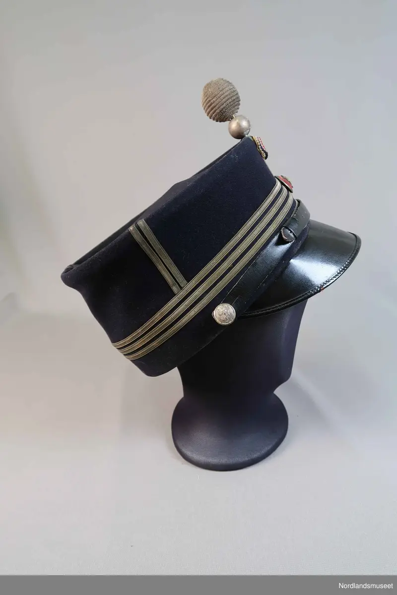 Uniformslue for politiet. Emaljert merke med riksløve. Skinnsnor. Den har en kule som sitter i front.