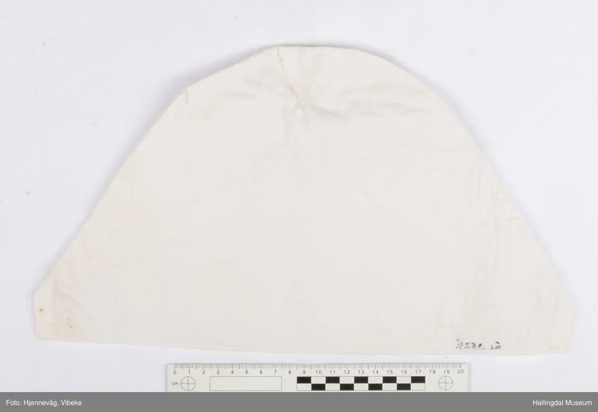 Bomullstoff og tråd. Sydd og brodert, hvitsøm. Rynket i nakken.