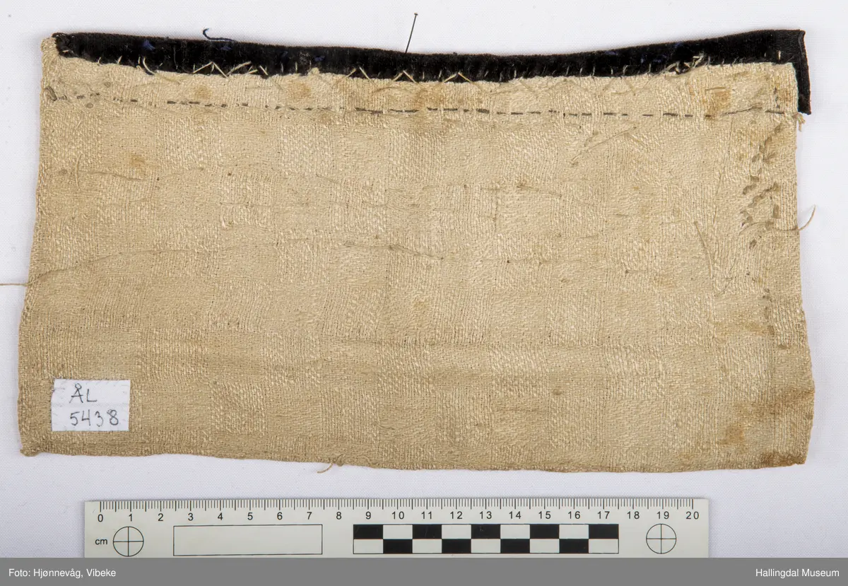 Brukt inni åpentrøye i Ålingsbunaden.  Klede, fløyelsbånd og perler. Perlenett. Sydd av rødt klede. Perler i svart, grønt, sennepsgult og kvitt. 4 store perler på midten. Kantet øverst med svart fløyelskant, 2,4 cm bredt. Sikksakkbånd av stavperler oppå fløyelskanten. Foret med linstoff i dreiel. Håndsydd. H: 14,5 cm, L: 26,5 cm.