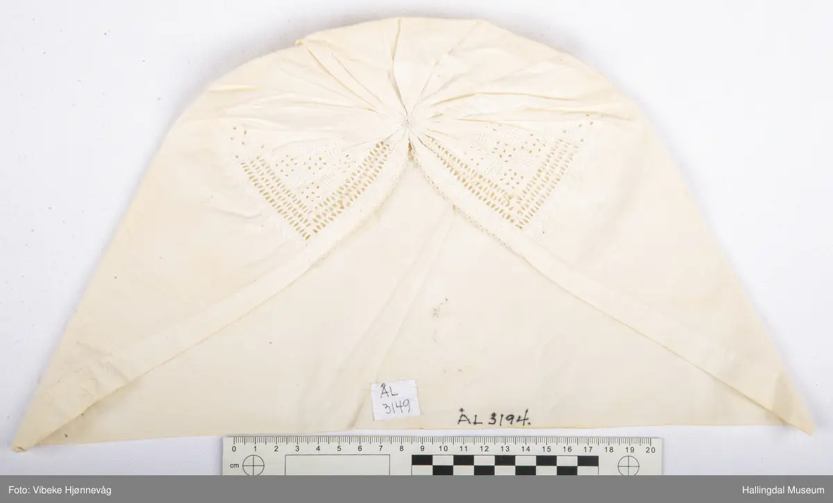 Bomullstoff, sydd og rynket. Kvitsaum med hullrad bak i nakken.