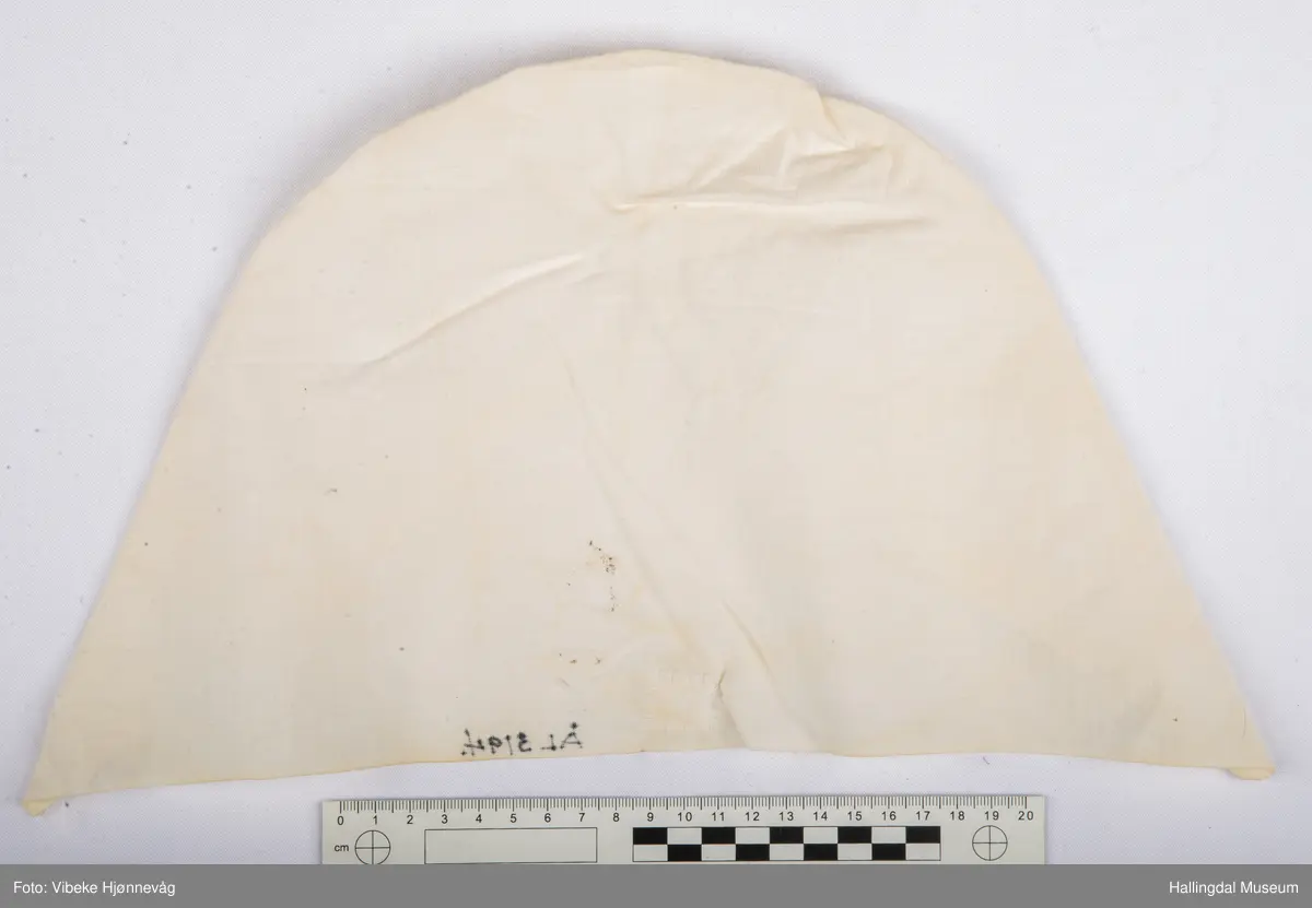 Bomullstoff, sydd og rynket. Kvitsaum med hullrad bak i nakken.