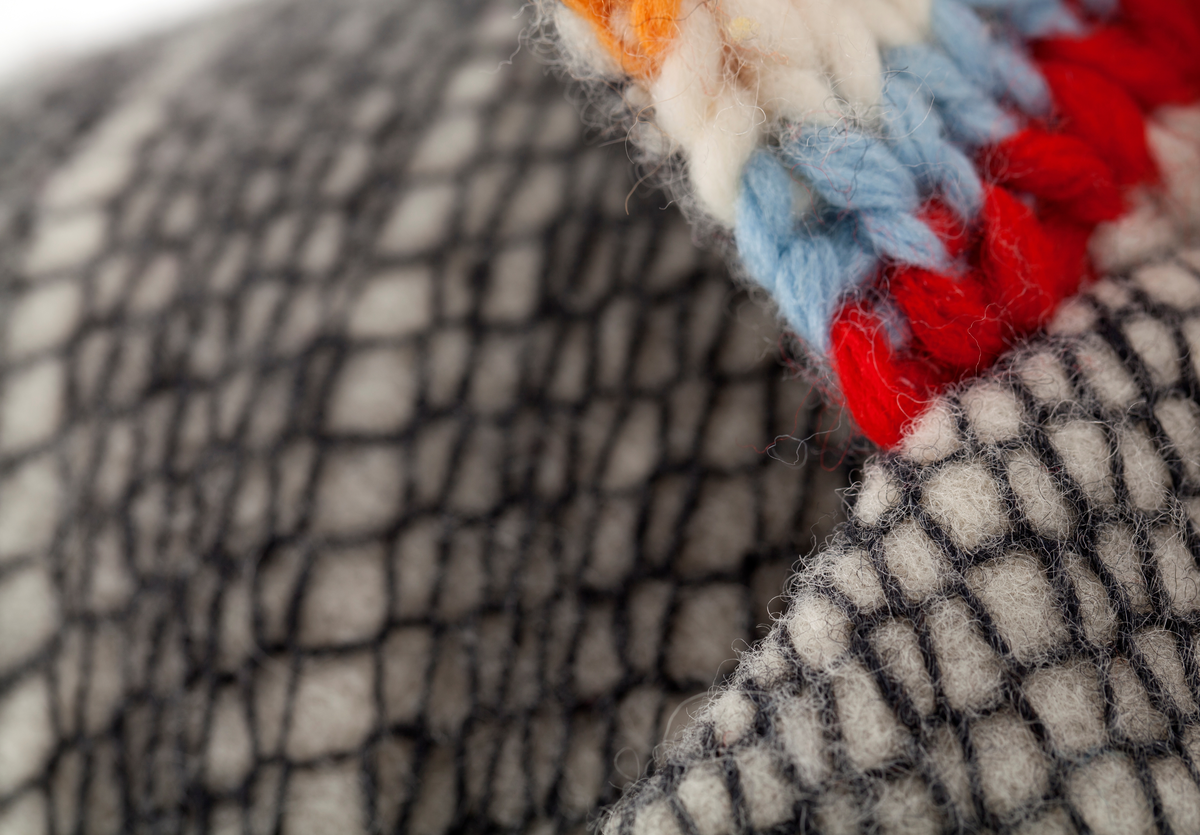 Dressjakke sydd av twool i koksgrå på hvit. Jakkens krage er strikket av tykt garn i ribbestrikk på tykke pinner i fargene (striper): oransje, gult, hvitt, lyseblått, rødt, gulbrunt og lysegrått.